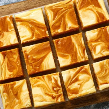 Swirled pumpkin cheesecake bars topped with whipped cream on a plate.