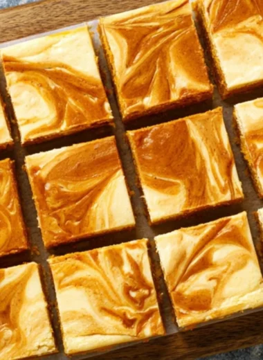 Swirled pumpkin cheesecake bars topped with whipped cream on a plate.