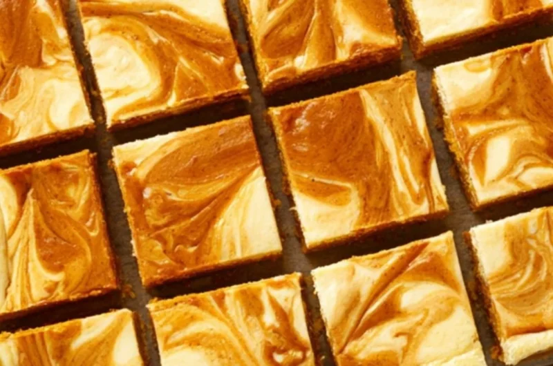 Swirled pumpkin cheesecake bars topped with whipped cream on a plate.
